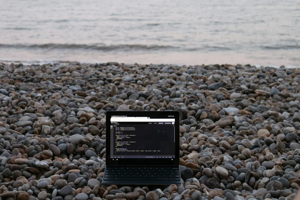 Laptop open on pebbles, facing the sea